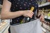 Woman stealing wine by placing the bottle into her handbag