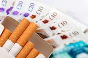 A packet of cigarettes set against a large amount of cash.