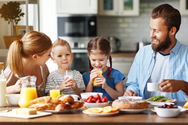Young family having breakfast of juice, milk, strawberries, bananas, and croissants.