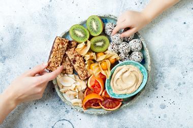 Hands reaching for plate with cereal bars, veg and energy balls