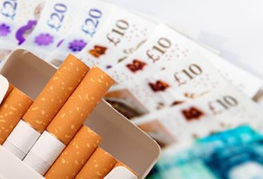 A packet of cigarettes set against a large amount of cash.