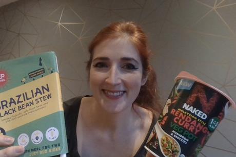 Smiling woman holding a vegan ready meal and veg pot.