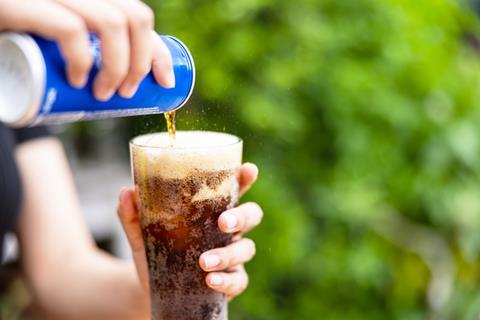 Close-up of hand pouring blue can of cola into glass on green background