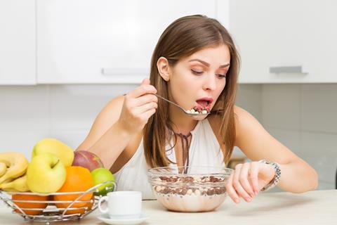 Woman eating bowl of cereal while looking at watch.