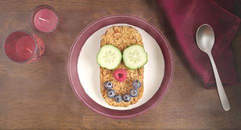 Bowl of Weetabix with smiley face made from cucumber slices and berries