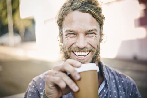 Man smiles broadly whilst holding coffee to go