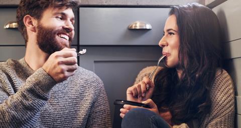 Couple share ice cream tub in kitchen