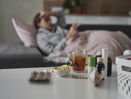 GettyImages_Woman laying under blanket with pills and medicines in foreground_Credit gpointstudio fit