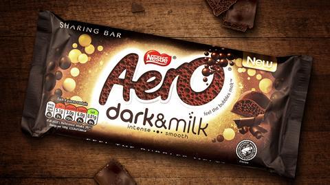 An Aero Dark & Milk block on a dark wooden surface with loose chunks of Aero chocolate.