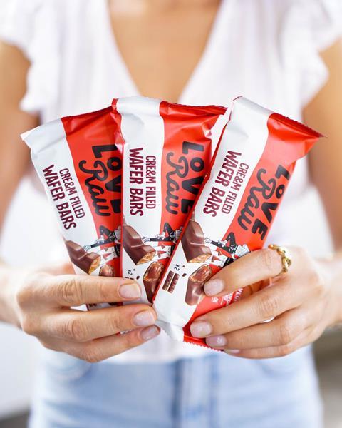 Hands holding vegan chocolate and cream wafer bar in red and white packaging.
