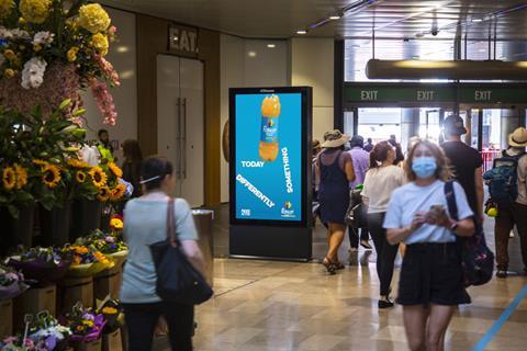 Masked commuters passing a digital screen featuring Rubicon