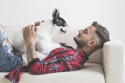 Young man in red checked shirt holding French bulldog.
