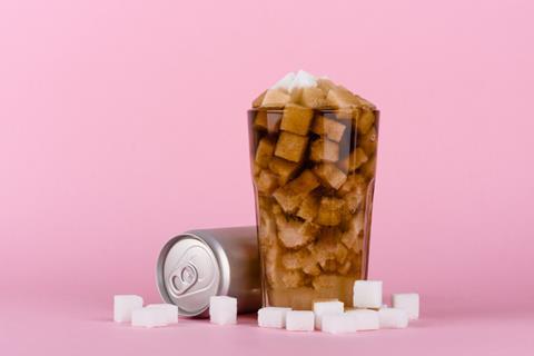 Glass of coke filled with sugar cubes and more sugar cubes on the surface