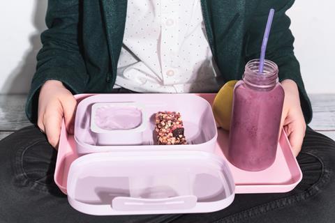 School kid holding pale pink plastic lunchbox with yoghurt and cereal bar