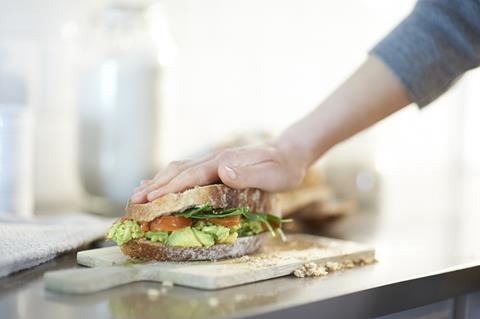 Hand pressing down on avocado sandwich on chopping board