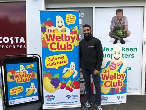 Retailer Anand Cheema stands with Healthy Living Scotland POS
