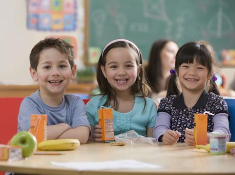 Three school children smiling with their juice drinks cartons and packed lunch