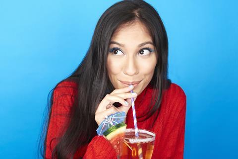 Long haired lady in red top sips fruity cocktail through a straw on bright blue background