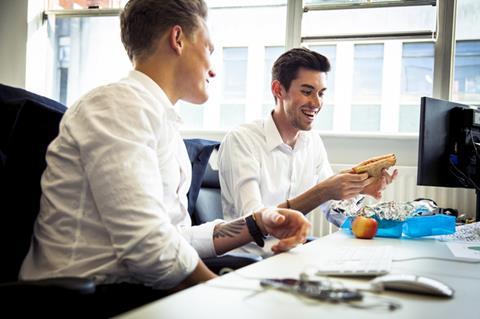 Man eating a packed lunch at his desk next to work colleague