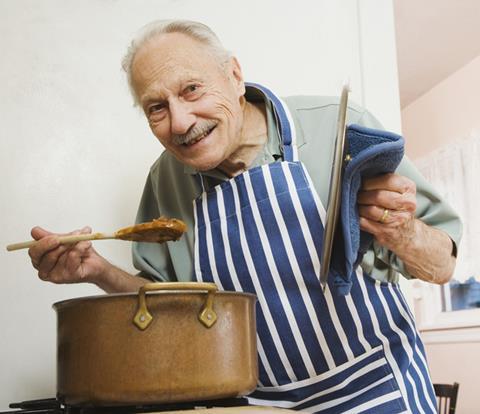 Elderly man holds wooden spoon above cooking pot