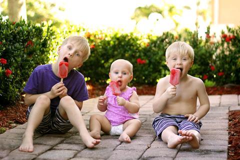 Three young children enjoying red lollies in the garden