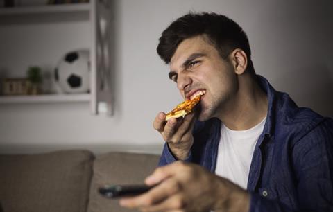 Man eating pizza and holding remote